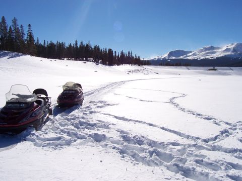 1994 Ford Bronco - Two snowmobiles are parked in a vast snowy landscape with mountains in the distance under a clear blue sky.