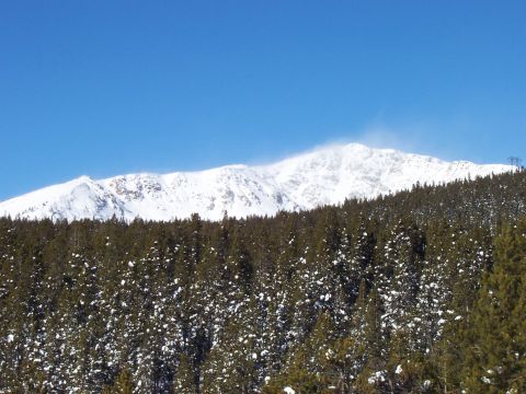 1994 Ford Bronco - A vast mountain range covered in snow looms over a dense forest of pine trees dusted with snow.