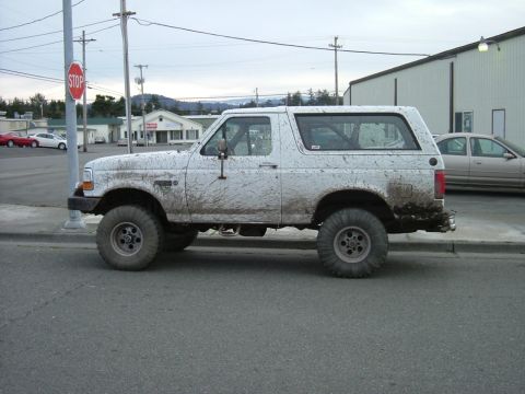 1993 Ford Bronco - This lifted Ford Bronco is heavily caked in mud, obscuring its original paint and condition.