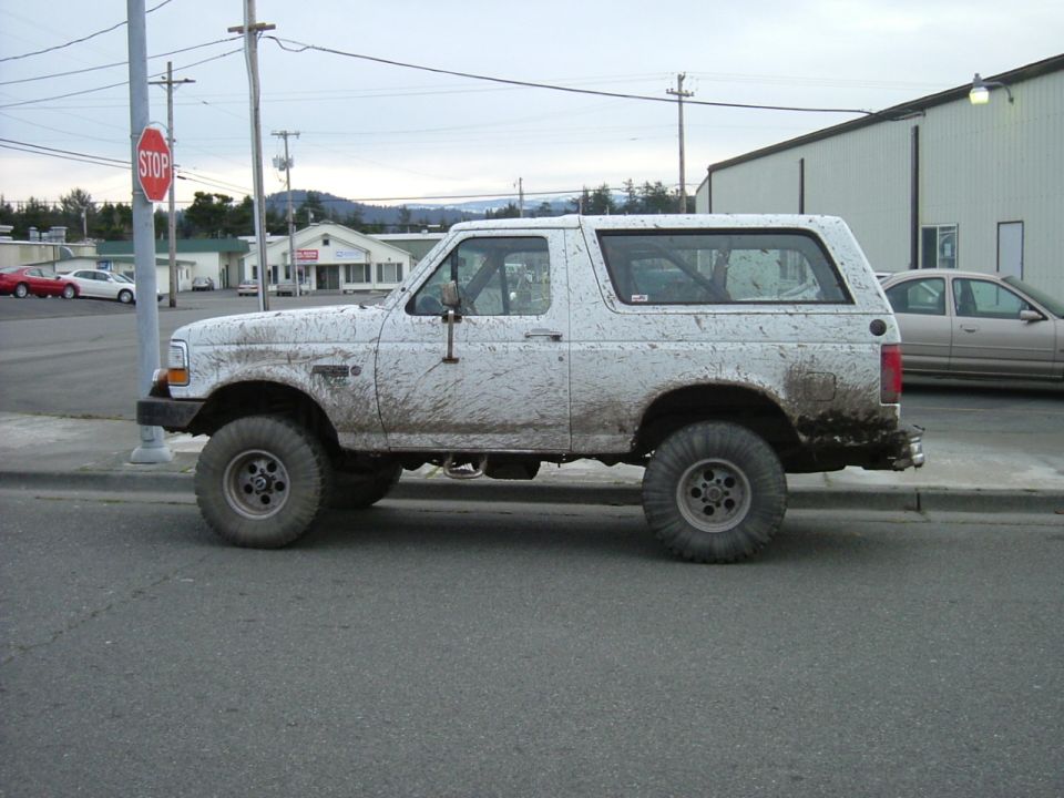 Mud-splattered white Ford Bronco, side view, lifted suspension, aftermarket wheels