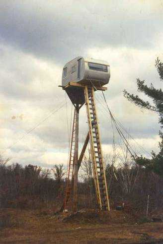 1979 Ford Bronco - A camper trailer is mounted high on stilts, accessible by ladders, in a wooded area.