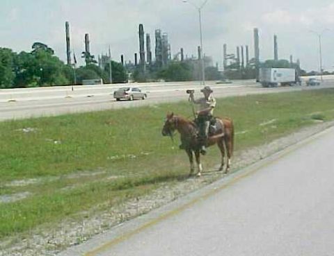 1979 Ford Bronco - Man on horseback beside highway with industrial complex in the distance.