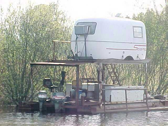 Homemade houseboat with a white camper shell on top, outboard motors