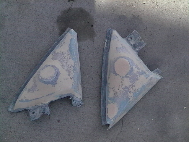 Two triangular car mirror housings, covered in primer and filler, sit on a concrete surface