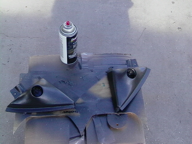 Two black plastic interior trim pieces and a can of spray paint on a cardboard surface