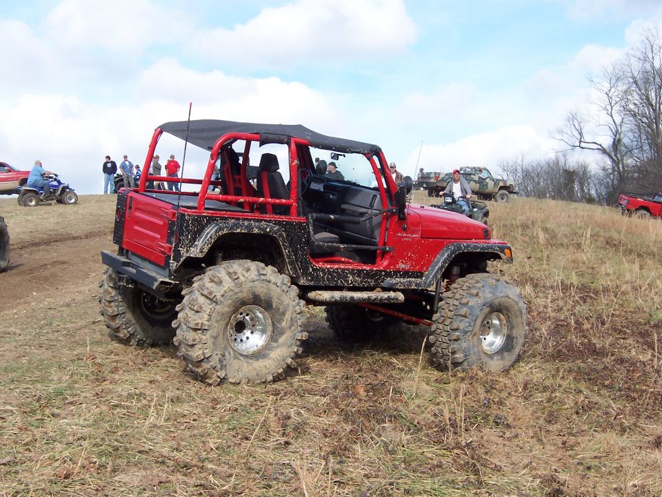 Red Jeep Wrangler on big mud tires and steel wheels at an off-road park