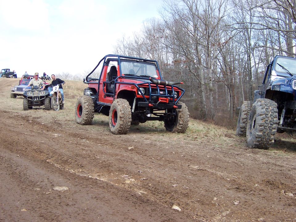 Red lifted buggy and other rigs lined up on a muddy off-road trail