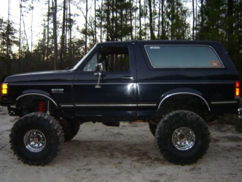 1989 Ford Bronco - This lifted Ford Bronco is parked outdoors with trees in the background. It features large tires and chrome wheels.