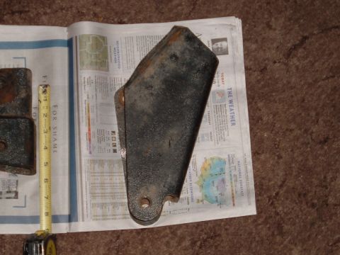 1994 Ford Bronco - Metal bracket and tape measure on newspaper. The tape measure has 'FOR SHAME' printed on it.