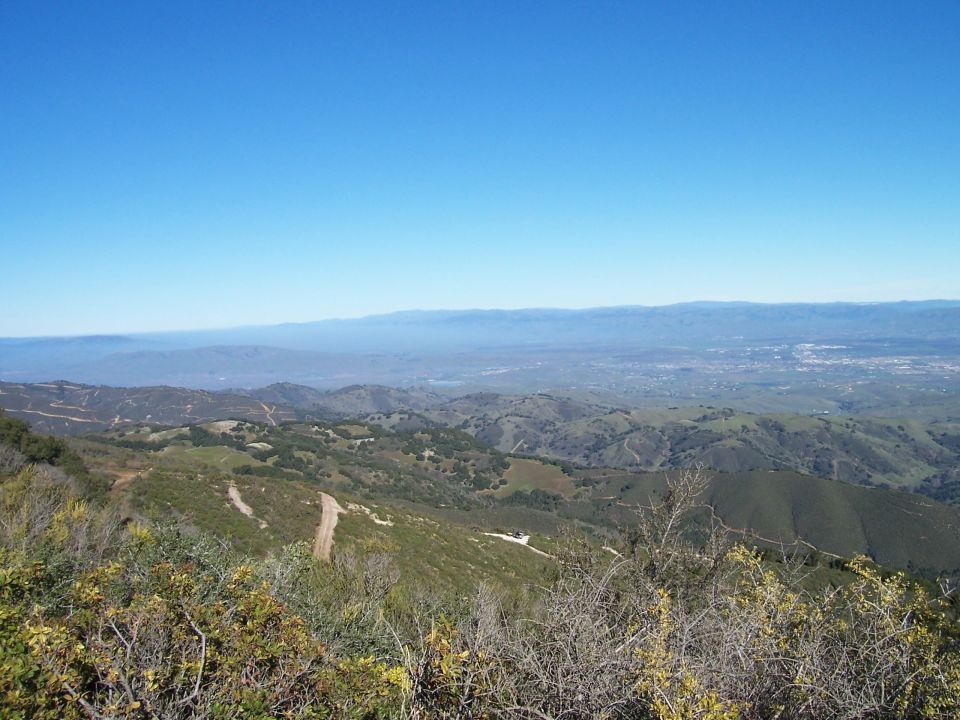 Overlook of a valley with distant city and mountains under a clear blue sky