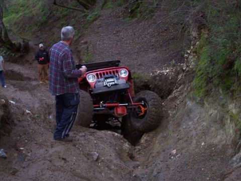 1998 Ford Ranger - A red Jeep is carefully driven through a challenging off-road obstacle on a dirt path.
