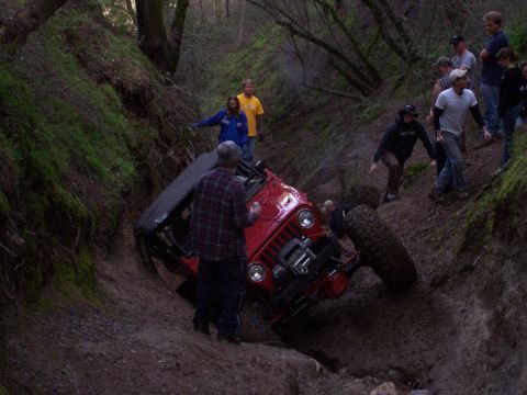 1998 Ford Ranger - A red off-road vehicle is stuck in a steep ditch while onlookers observe from the embankment.