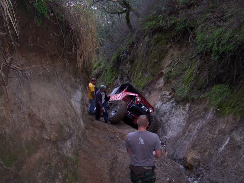 1998 Ford Ranger - A red off-road Jeep navigates a challenging, narrow dirt path with onlookers observing the difficult terrain.