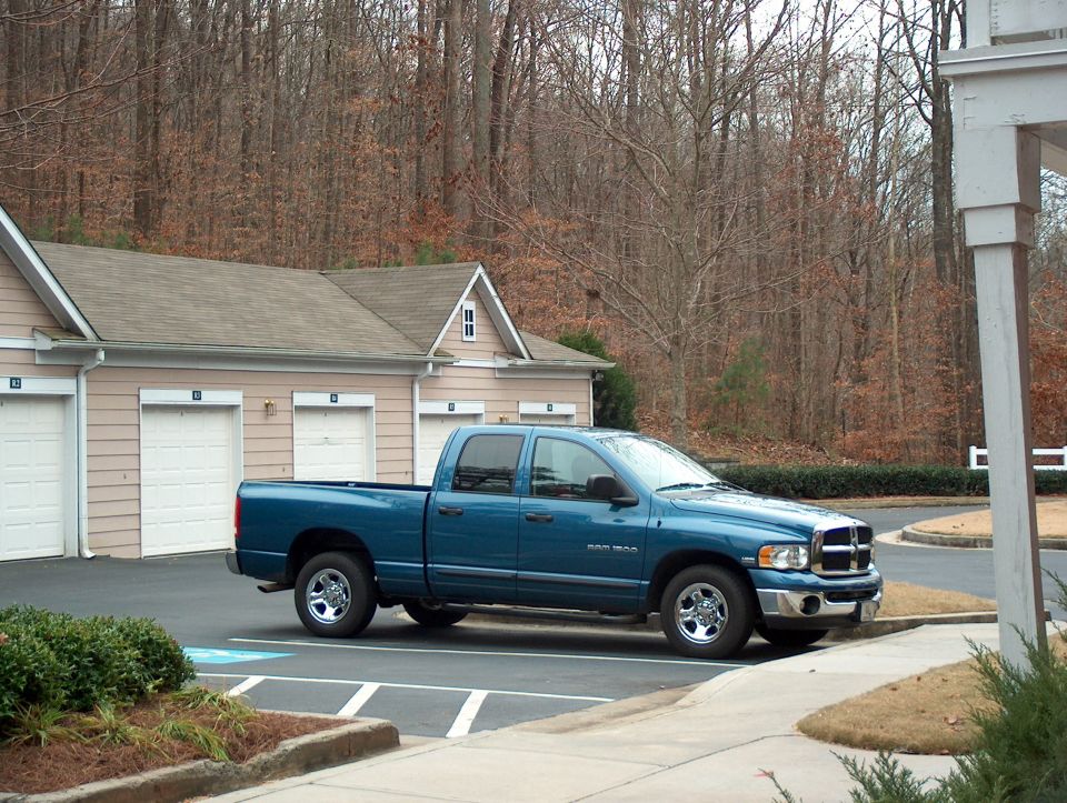 Blue 2004 Dodge 1500 pickup truck parked in front of a building with garages