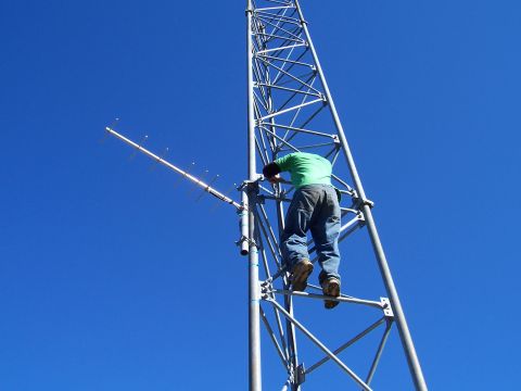 1998 Ford Ranger - A worker ascends a large radio tower under a clear blue sky, working on attached antennas.