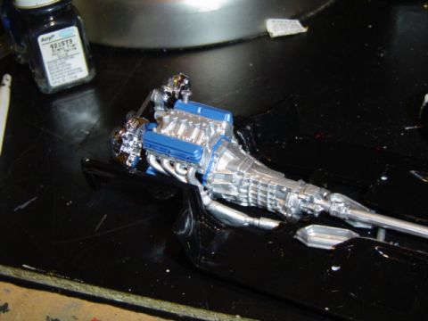 1979 Ford Bronco - A detailed model engine and transmission assembly sits on a black surface, with a bottle of acrylic paint nearby.