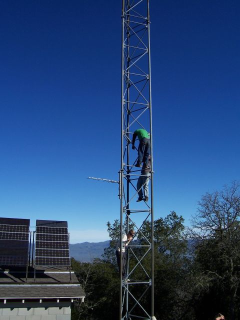 1998 Ford Ranger - Workers ascend a tall metal tower against a clear blue sky, with solar panels visible on a nearby roof.