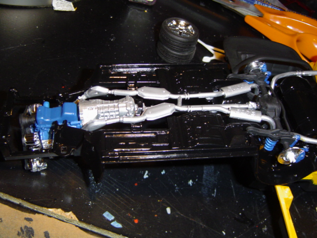 model car chassis with blue engine and silver exhaust system, plus a separate tire