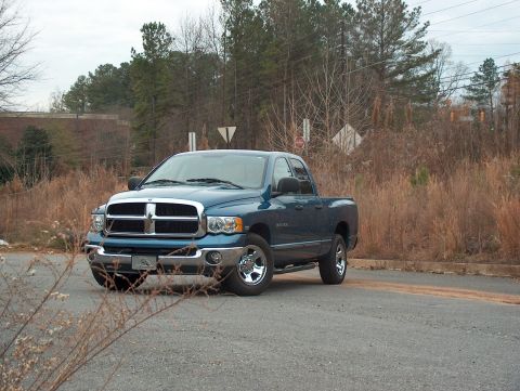 2004 Dodge 1500 - A blue 2004 Dodge 1500 pickup truck is parked on a road with dry vegetation and trees.