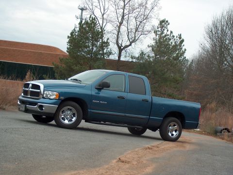 2004 Dodge 1500 - A blue 2004 Dodge 1500 pickup truck is shown from a 3q-front angle, parked on an asphalt surface with trees and a building in the backgroun…