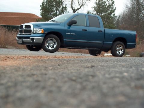 2004 Dodge 1500 - A blue Dodge Ram pickup truck is parked on a dirt road with a building and trees in the background.