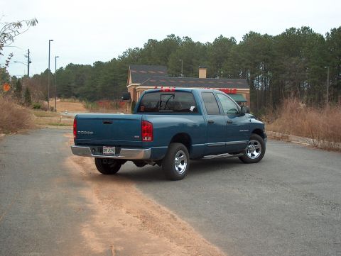 2004 Dodge 1500 - A blue Dodge Ram pickup truck is parked on a paved road with trees and a building in the background.
