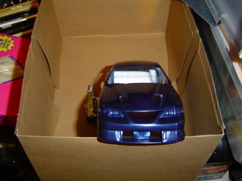 1979 Ford Bronco - Model car sits inside a cardboard box, with a pink box and other items in the background.