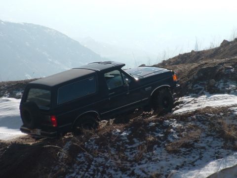 1991 Ford Bronco - Black Ford Bronco navigates a challenging off-road terrain with snow and mud.