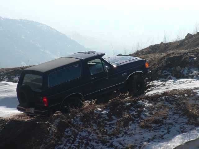 Black Ford Bronco with aftermarket wheels driving on a snowy, muddy hill
