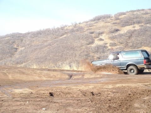 1991 Ford Bronco - A Ford Bronco navigates a muddy terrain, sending dirt flying.