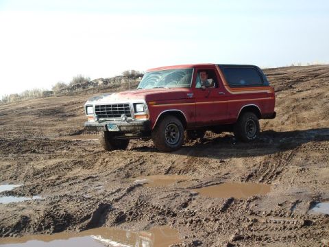 1991 Ford Bronco - This red 1978 Ford Bronco navigates a muddy terrain, showing off its off-road capabilities.