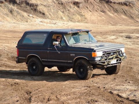1991 Ford Bronco - 1991 Ford Bronco with aftermarket bumper driving on dirt terrain.