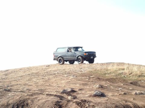 1991 Ford Bronco - A gray Ford Bronco is parked on a dirt hill under a bright sky.
