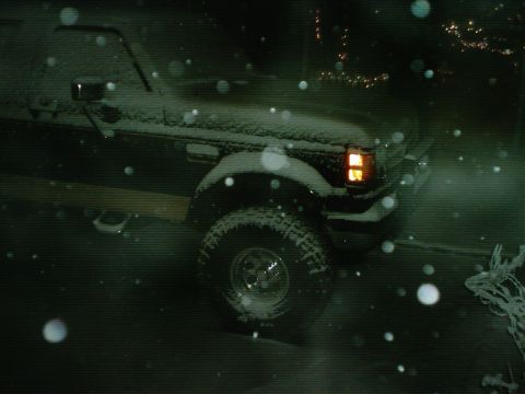 1989 Ford Bronco - A dark colored Ford F-Series truck is parked outside during a snowfall at night.