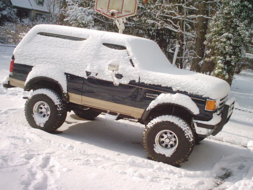 Dark blue and tan Ford Bronco covered in snow, parked on a snowy driveway
