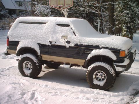 1989 Ford Bronco - A dark blue and tan Ford Bronco is covered in snow, parked outside in a winter scene.