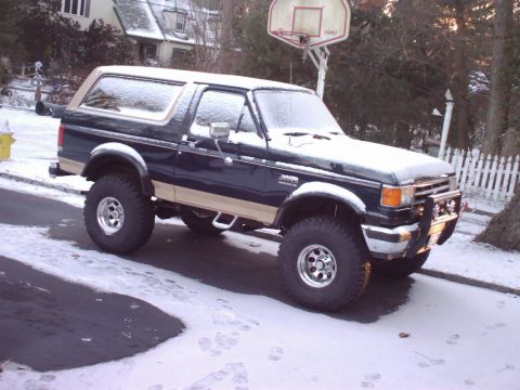 1989 Ford Bronco - Dark blue 1989 Ford Bronco with tan trim sits covered in snow on a residential street.