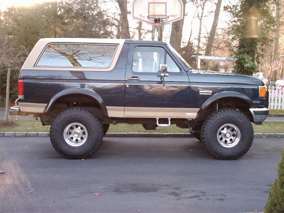 Dark blue and tan Ford Bronco with aftermarket wheels, seen from the side
