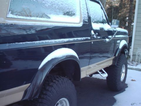 1989 Ford Bronco - A dark blue and tan 1989 Ford Bronco is partially covered in snow, viewed from the 3/4 front angle.