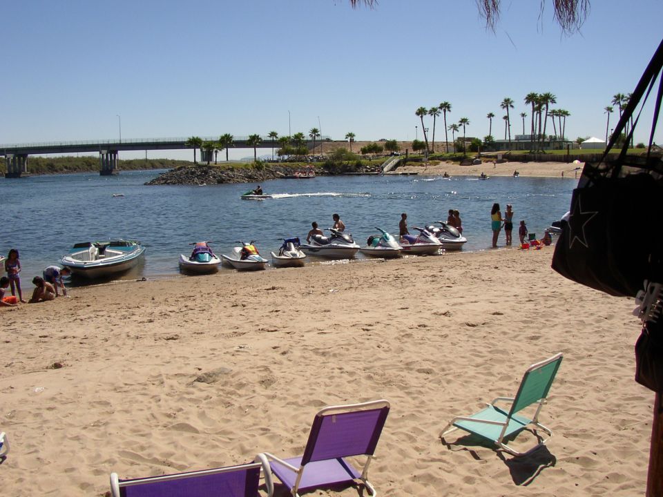 Beach with personal watercraft and a boat lined along the shore by a river and bridge