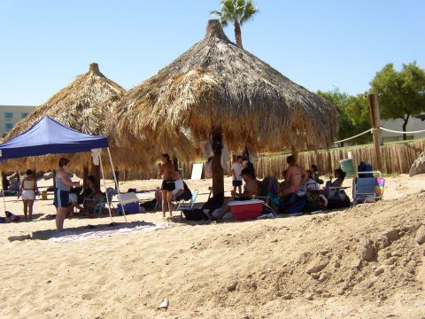 1990 Ford Bronco - Beachgoers enjoy the shade on a sunny day under thatched umbrellas and a blue canopy.