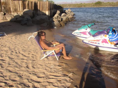 1990 Ford Bronco - woman lounges in a beach chair on the sand next to two jet skis beached at the water's edge in evening light.