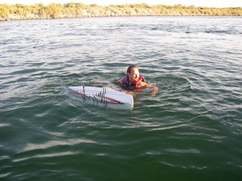 1990 Ford Bronco - child wearing a life vest swims in open lake water while holding onto a white board, with a brushy shoreline behind.