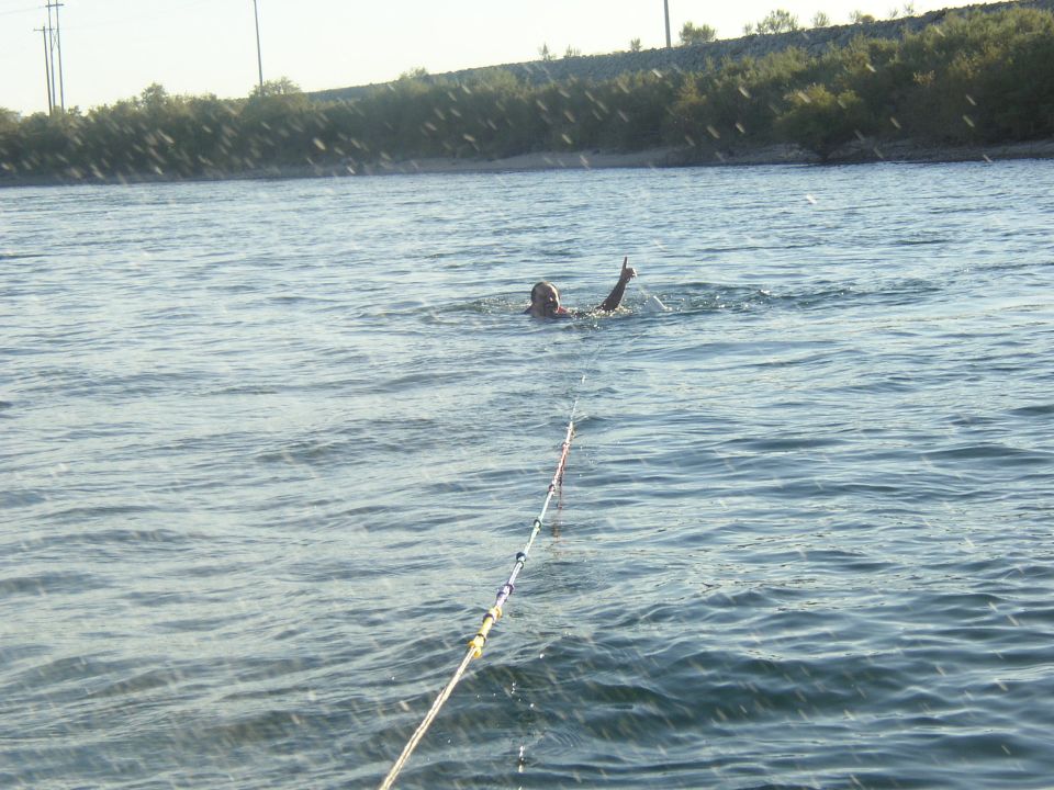 Person in the water at the end of a tow rope on a lake with a low green shoreline behind