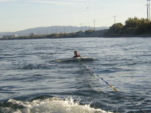 1990 Ford Bronco - person sits in the water gripping a ski tow rope amid the boat wake, with distant mountains and power lines behind.