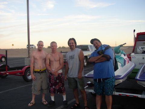 1990 Ford Bronco - Four men stand together for a photo in a parking lot next to a jet ski on a red trailer as the sky fades to dusk.