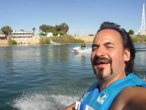 1990 Ford Bronco - grinning man in a blue life vest takes a selfie on the water while a jet ski rider follows behind on the river.