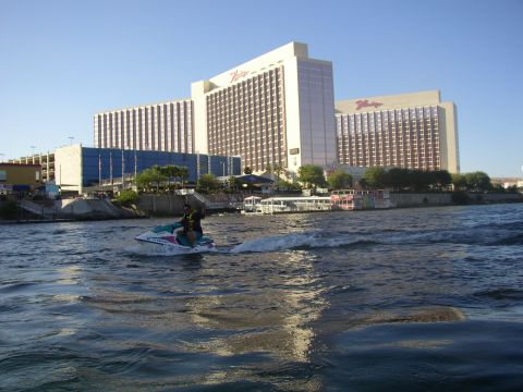 1990 Ford Bronco - rider on a teal-and-white jet ski crosses choppy river water in front of a large white casino resort on the far shore.