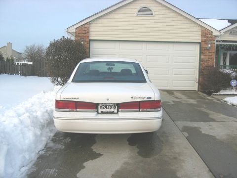 1997 Ford Crown Victoria - Rear view of a white 1997 Ford Crown Victoria in front of a garage on a snowy day.