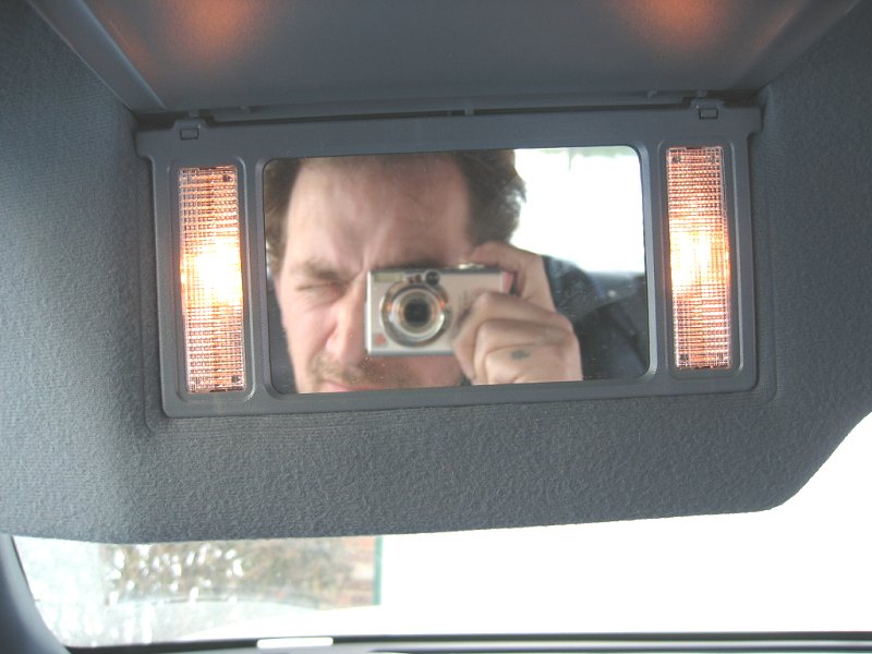 Man photographing himself in overhead console vanity mirror of vehicle